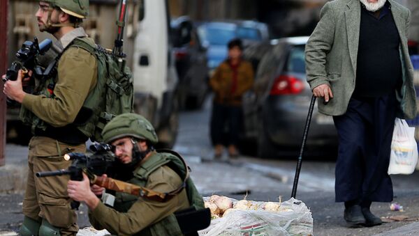 رجل فلسطيني ينظر إلى جندي إسرائيلي يستهدف مظاهرة في الخليل بالضفة الغربية التي تحتلها إسرائيل - سبوتنيك عربي