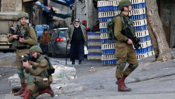 رجل فلسطيني يمشي بينما يطلق جندي إسرائيلي سلاحه خلال احتجاج على خطة الرئيس الأمريكي دونالد ترامب للسلام في الشرق الأوسط في الخليل في الضفة الغربية التي تحتلها إسرائيل - سبوتنيك عربي