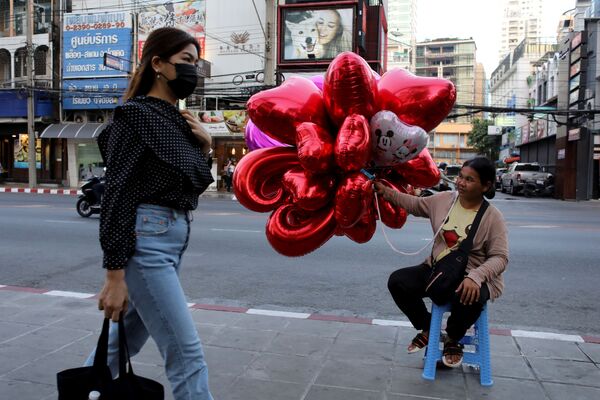 امرأة ترتدي قناعا واقيا تسير على خلفية بلالين على شكل قلوب حمراء في بانكوك، تايلاند 14 فبراير 2020 - سبوتنيك عربي