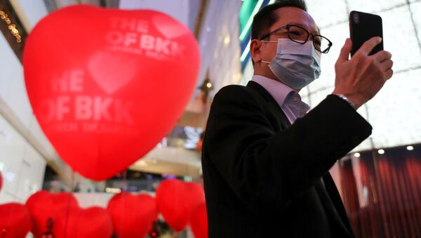 رجل يرتدي قناعا واقيا يلتقط صورة سيلفي على خلفية بلالين على شكل قلوب حمراء بمناسبة يوم فالنتاين (عيد الحب) في بانكوك، تايلاند 13 فبراير 2020 - سبوتنيك عربي