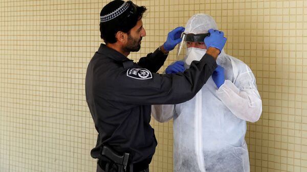 ضابط في الشرطة الإسرائيلية يساعد مفتش صحة على ارتداء معدات واقية من كورونا - إسرائيل - سبوتنيك عربي