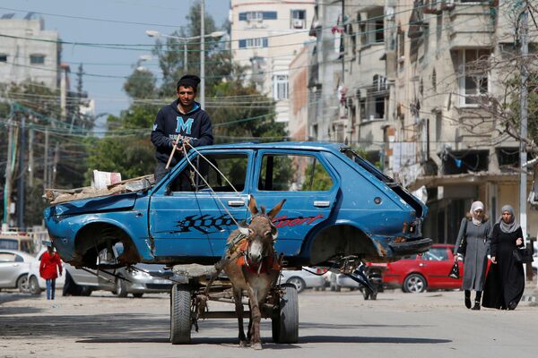 فلسطيني يركب عربة يجرها الحمار تنقل سيارة قديمة إلى ساحة للخردة، في مدينة غزة، 15 مارس، 2020. - سبوتنيك عربي