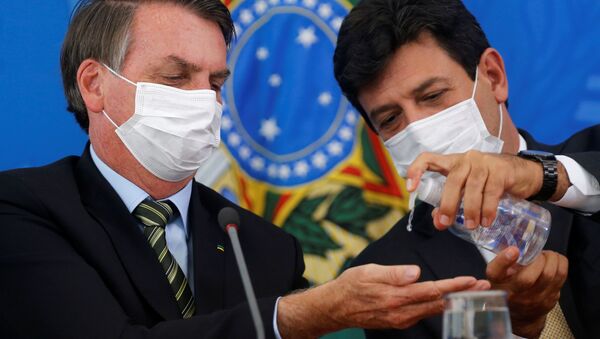 الرئيس البرازيلي جاير بولسونارو ووزير الصحة لويز إنريكي مانديتاس، يرتديان أقنعة واقية، ويعقمان أيديهما خلال مؤتمر صحفي للإعلان عن اجراءات احترازية للحد من انتشار مرض الفيروس التاجي (COVID-19) في البرازيل، البرازيل، 18 مارس 2020. - سبوتنيك عربي