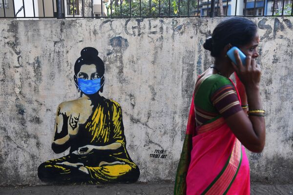 امرأة تسير على خلفية رسم غرافيتي لبوذا يرتدي قناعا واقيا، مومباي، الهند 16 مارس 2020 - سبوتنيك عربي