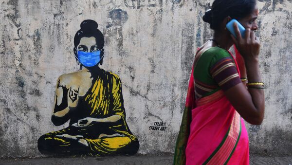 امرأة تسير على خلفية رسم غرافيتي لبوذا يرتدي قناعا واقيا، مومباي، الهند 16 مارس 2020 - سبوتنيك عربي