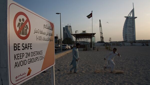 عاملان يلعبان بالقرب من لافتة تحذر الناس بضرورة الحفاظ على مسافة من بعضهم البعض عند تفشي الفيروس التاجي الجديد أمام فندق برج العرب الفاخر على شكل شراع في دبي - سبوتنيك عربي