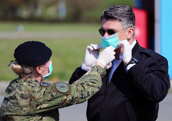 جندي يساعد الرئيس الكرواتي زوران ميلانوفيتش على ارتداء قناع للوجه قبيل زيارته الخيام التي تم إنشاءها لمرضى الفيروس التاجي (COVID-19) في مستشفى دوبرافا في زغرب، كرواتيا 21 مارس 2020. - سبوتنيك عربي