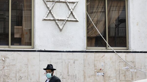 رجل متشدد يمشي بالقرب من كنيس يهودي في شارع مهجور بسبب الإجراءات الحكومية للمساعدة في وقف انتشار فيروس كورونا في بني براك إحدى ضواحي تل أبيب في إسرائيل  - سبوتنيك عربي