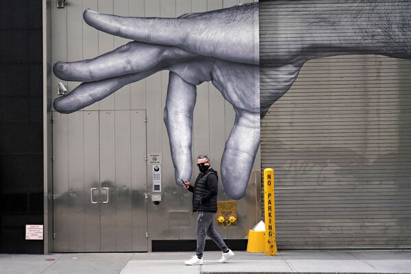 رجل يرتدي قناعاً واقياً يسير بجوار فن الشارع وسط انتشار الجائحة، فيروس كورونا في مدينة نيويورك، 5 أبريل 2020 - سبوتنيك عربي