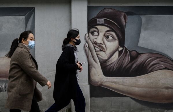 أشخاص يرتدون أقنعة واقية يمشون أمام جدارية على طول شارع في مدينة ووهان بمقاطعة هوبي وسط الصين، 2 أبريل 2020 - سبوتنيك عربي