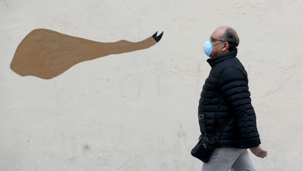 رجل يرتدي قناعا وقفازات واقية يسير على خلفية رسم غرافيتي لساق لحم خنزير الإيبيري (المشهورة في إسبانيا) أثناء الإغلاق التام، على خلفية انتشار مرض كوفيد-19 في مدريد، إسبانيا 6 أبريل 2020. - سبوتنيك عربي