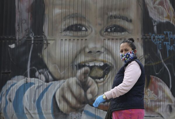 امرأة ترتدي القناع الواقي وقفازات، تسير على خلفية لوحة جدارية في سواتشا، على مشارف مدينة بوغوتا في كولومبيا، 1 أبريل 2020 ، أثناء إغلاق تام على مستوى الدولة لأنها تسعى لمنع انتشار كوفيد-19. - سبوتنيك عربي