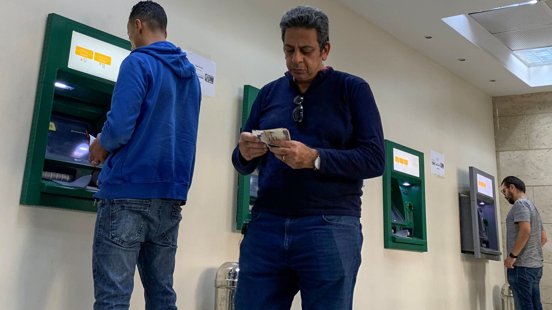 رجل يحسب أمواله بينما يستخدم الآخرون أجهزة الصراف الآلي في البنك الأهلي المصري حيث تكثف مصر جهودها لإبطاء انتشار فيروس كورونا - سبوتنيك عربي, 1920, 28.10.2021