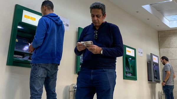 رجل يحسب أمواله بينما يستخدم الآخرون أجهزة الصراف الآلي في البنك الأهلي المصري حيث تكثف مصر جهودها لإبطاء انتشار فيروس كورونا - سبوتنيك عربي