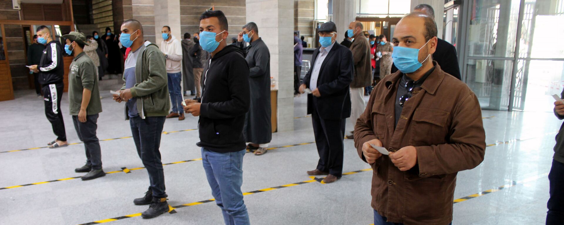 مواطنون يرتدون كمامات طبية كجزء من اجراءات وقائية مرض فيروس كورونا (كوفيد-19)، وهم يقفون على بعد مسافة آمنة وفق معايير منظمة الصحة العالمية، في طوابير في أحد البنوك في مصراتة، ليبيا  22 مارس / آذار 2020 - سبوتنيك عربي, 1920, 31.07.2021