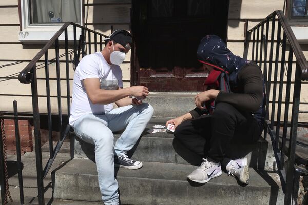 رجلان يرتديان أقنعة واقية يلعبان الورق أمام المنزل في بروكلين، نيويورك  2أبريل 2020 - سبوتنيك عربي