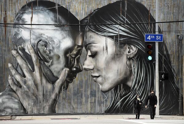 أشخاص يرتدون الكمامات وهم يعبرون الشارع أمام جدارية في حي الفنون في لوس أنجلوس، حيث تستمر أوامر البقاء في المنزل في كاليفورنيا بسبب الفيروس التاجي كورونا، 10 أبريل 2020. - سبوتنيك عربي