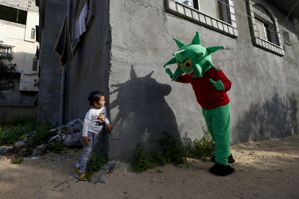 رجل فلسطيني يرتدي زي يشبه الفيروس التاجي كورونا، مخيط من قبل أخته، يلعب مع طفلة وسط قطاع غزة خلال جائحة كوفيد-19، 20 أبريل  2020. - سبوتنيك عربي