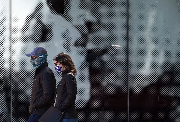 ثنائي يرتدي كمامات واقية يسيران على خلفية لوحة إعلانية لدار السينما، وسط جائحة فيروس كورونا في واشنطن العاصمة، في 22 أبريل 2020. - سبوتنيك عربي