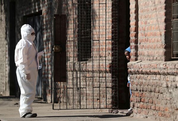 امرأة ترتدي بدلة واقية تتحدث إلى طفل في حي للمهاجرين، أثناء بدء الحجر الصحي العام، بسبب الأعداد المتزايدة من حالات الإصابة بفيروس كورونا في مدينة سانتياغو، تشيلي 16 مايو 2020. - سبوتنيك عربي