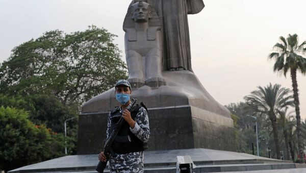 شرطي مصري يرتدي قناع وجه واقٍ يقف بجانب تمثال نهضة مصر خلال شهر رمضان حيث تكثف مصر جهودها لإبطاء انتشار فيروس كورونا - سبوتنيك عربي