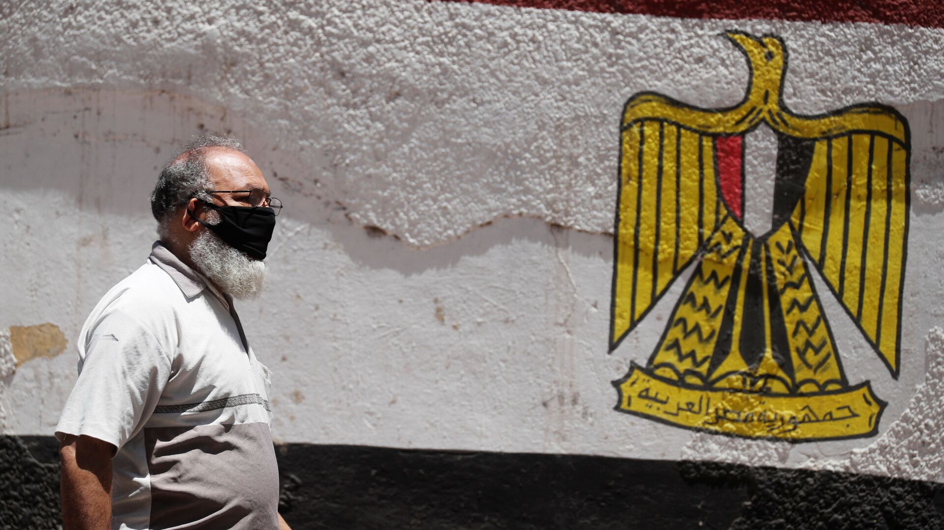 رجل يرتدي قناع الوجه الواقي لمنع انتشار مرض فيروس كورونا (COVID-19) يمشي بجوار جدار مطلي بألوان علم مصر في وسط القاهرة - سبوتنيك عربي, 1920, 05.03.2021