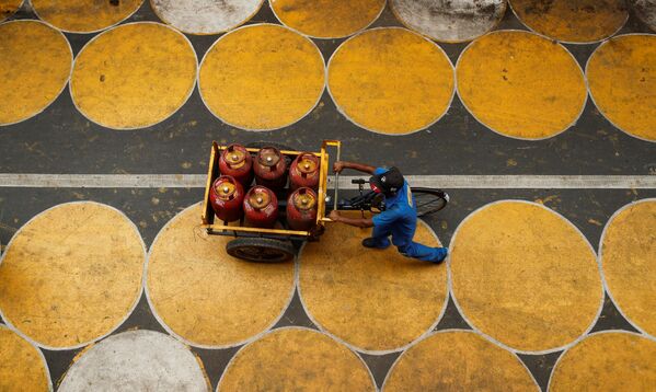 رجل يدفع عربة مملوءة بأسطوانات غاز البترول المسال في شارع فيه دوائر للمارة للحفاظ على التباعد الاجتماعي بعد تخفيف بعض القيود بعد إغلاق تام فرض لإبطاء انتشار مرض (COVID-19) في مومباي، الهند، 1 يوليو 2020. - سبوتنيك عربي