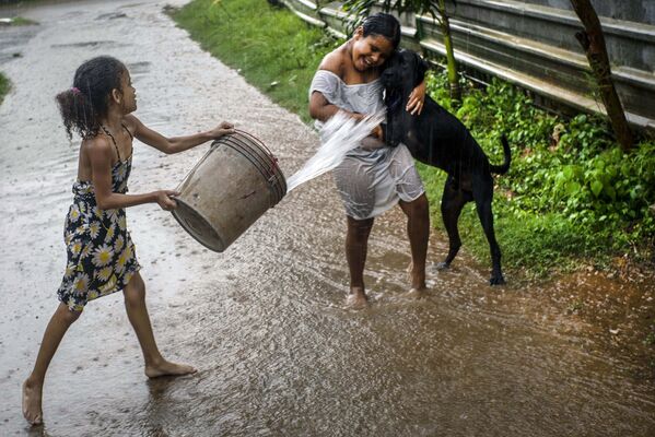 فتاة تلقي الماء على صديقتها وهي تلعب تحت المطر في هافانا، كوبا، 1 يوليو 2020. - سبوتنيك عربي